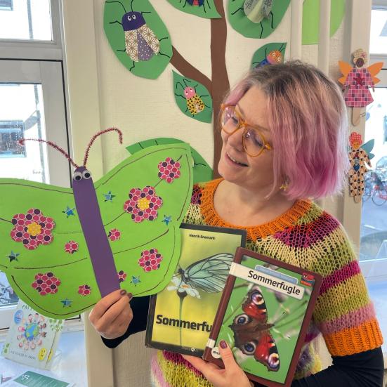 Lotte står med 2 bøger og en papirsommerfugl