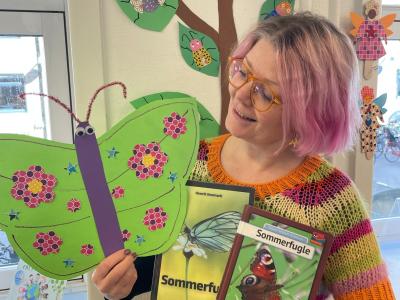 Lotte står med 2 bøger og en papirsommerfugl