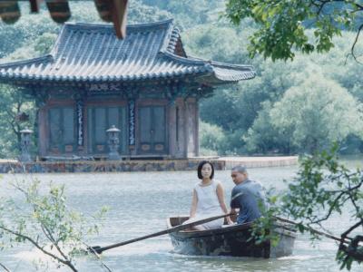 Mand og kvinde i en båd på en sø, foran et koreansk hus.