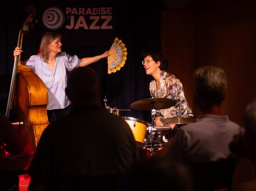 Bassisten i Sophisticated Ladies vifter trommeslageren under en sommervarm koncert i HUSET i 2026.