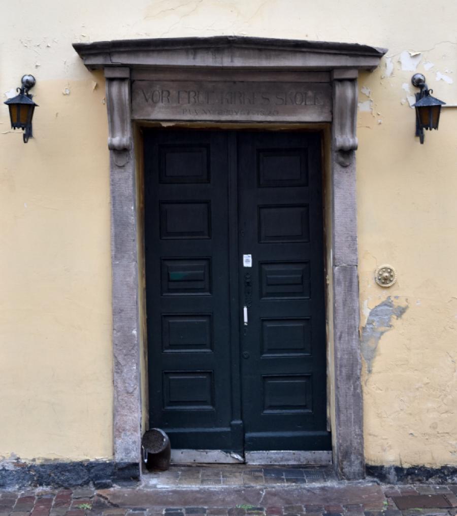 Dør med portal og teksten "VOR FRUE KIRKES SKOLE / PAA NY OPBYGT 1820"