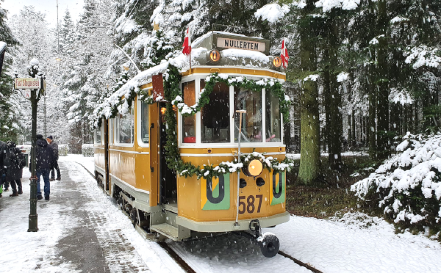 En julepyntet sporvogn ved en perron i et snebeklædt skovlandskab
